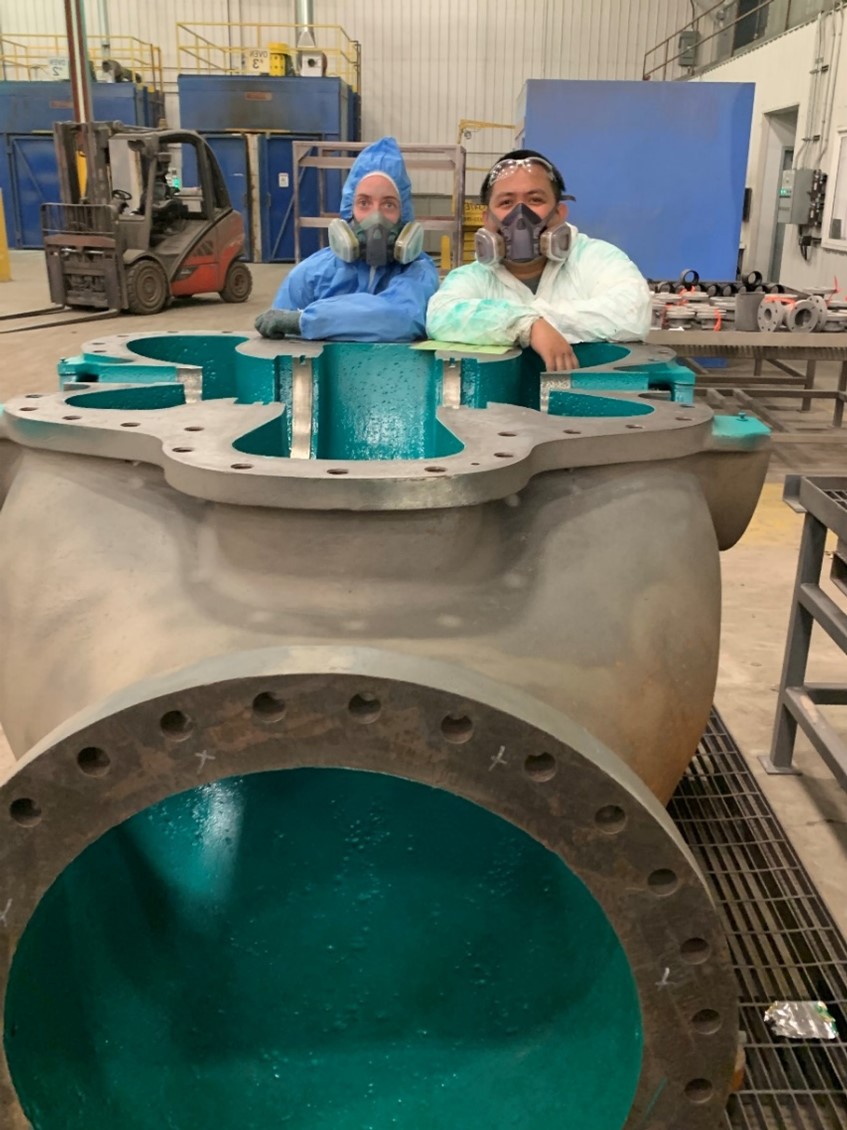 Two coating applicators standing beside giant pipe